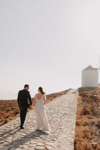 couple walking towards a windmill in astypalaia island Greece